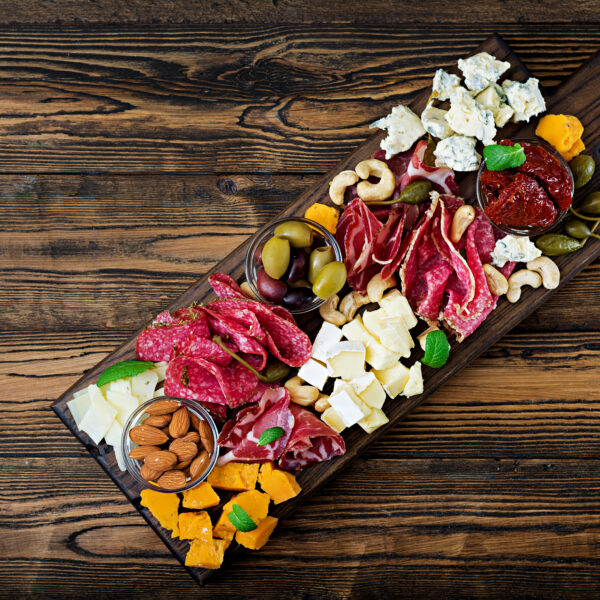 Antipasto catering platter with bacon, jerky, sausage, blue cheese and grapes on a wooden background. Top view
